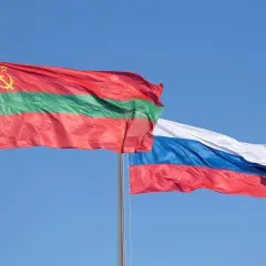Dwie flagi powiewają na wietrze: flaga niebiesko czerwona z białym, niebieskim i czerwonym pasem oraz flaga z czerwonym, zielonym i czerwonym pasem, ozdobiona sierpem i młotem.