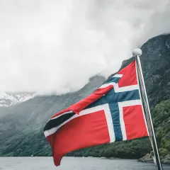 Flaga Norwegii powiewa na maszcie na tle malowniczego fiordu.