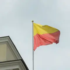 Flaga Warszawy powiewa na maszcie obok zabytkowego budynku.