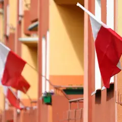 Kilka biało-czerwonych flag państwowych powiewa na tle pomarańczowo-żółtego budynku.