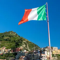 Flaga Włoch powiewa na tle błękitnego nieba nad kolorowymi domkami Cinque Terre.