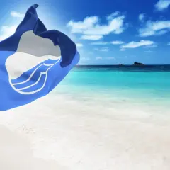 Niebieska flaga powiewa na wietrze na tle turkusowego morza i białej plaży. Idealne miejsce na wakacje.