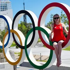Kobieta w czerwonej koszulce z polską flagą siedzi na jednym z kół symbolizujących flagę olimpijską.