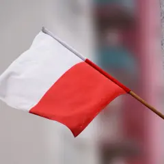 Flaga Polski powiewa na wietrze, biało-czerwona, ale w odwrotnej kolejności.