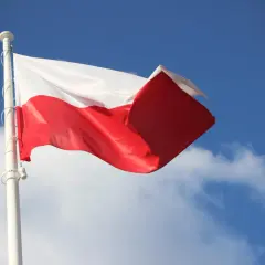 Biało-czerwona flaga Polski powiewa na maszcie na tle błękitnego nieba z chmurami. To symbol ważnych dat, kiedy wywieszamy flagę.