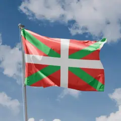 Flaga Basków (Ikurriña) powiewa na tle błękitnego nieba z chmurami.
