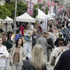 Tłum ludzi spaceruje ulicą z kramami i namiotami, ozdobioną flagami.