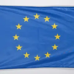 Niebieska flaga z dwunastoma złotymi gwiazdami ułożonymi w okrąg. To godło Unii Europejskiej, symbol jedności i solidarności.