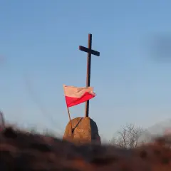 Na kamieniu, pod krzyżem, powiewa biało-czerwona flaga Polski.