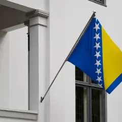 Flaga Bośni i Hercegowiny powiewa na tle białej ściany.