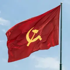 Czerwona flaga z sierpem i młotem, symbol ZSRR, powiewa na maszcie na tle błękitnego nieba z chmurami.