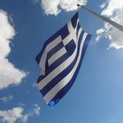 Flaga Grecji powiewa na tle błękitnego nieba z chmurami.