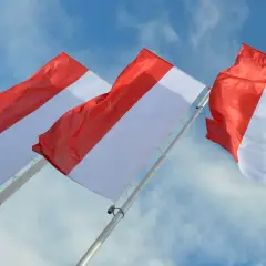 Trzy biało-czerwone flagi powiewające na tle błękitnego nieba z chmurami.