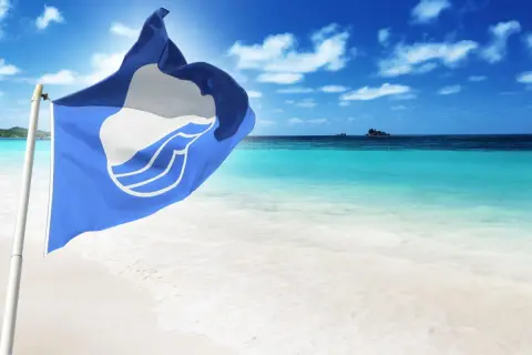 Niebieska flaga powiewa na wietrze na tle turkusowego morza i białej plaży. Idealne miejsce na wakacje.