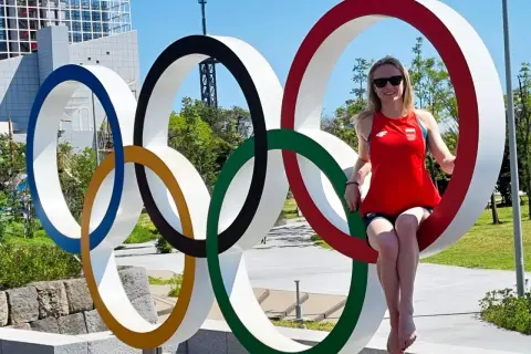 Kobieta w czerwonej koszulce z polską flagą siedzi na jednym z kół symbolizujących flagę olimpijską.