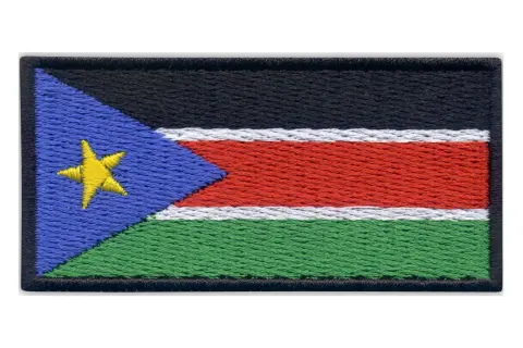 Naszywka z flagą Sudanu Południowego. Czarny pas na górze, pod nim biały, czerwony i zielony pas. Z lewej strony niebieski trójkąt z żółtą gwiazdą.