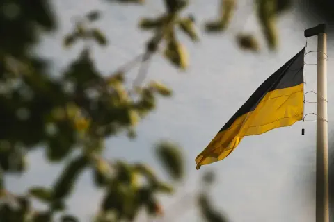 Flaga czarno żółta powiewa na maszcie, na tle nieba i rozmytych liści.