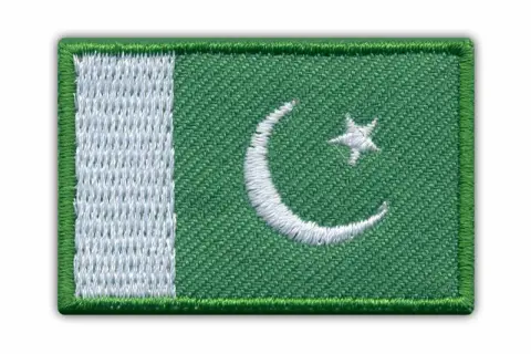 Naszywka z flagą Pakistanu. Zielone tło z białym półksiężycem i gwiazdą, oraz pionowym białym pasem po lewej stronie.