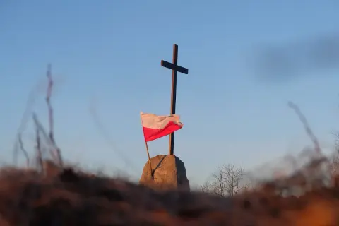 Na kamieniu, pod krzyżem, powiewa biało-czerwona flaga Polski.