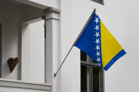 Flaga Bośni i Hercegowiny powiewa na tle białej ściany.