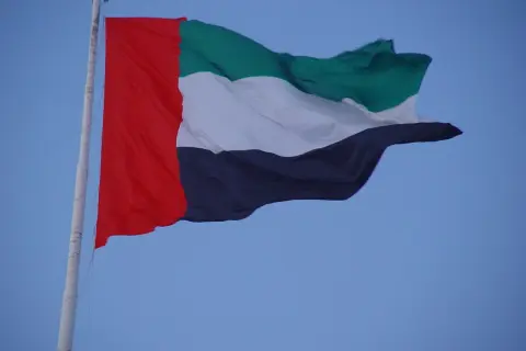 Flaga Zjednoczonych Emiratów Arabskich, znana również jako flaga Dubaju, powiewa na maszcie na tle błękitnego nieba.