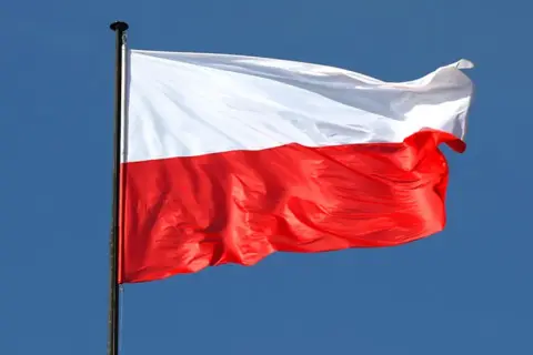 Biało-czerwona flaga Polski powiewa na maszcie na tle błękitnego nieba. Czy flaga może wisieć cały rok? Tak, symbol dumy narodowej jest zawsze na miejscu.