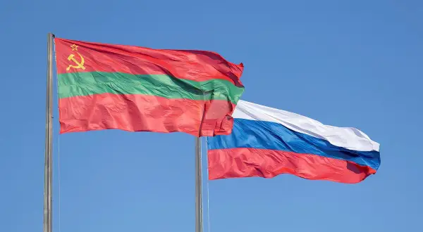 Dwie flagi powiewają na wietrze: flaga niebiesko czerwona z białym, niebieskim i czerwonym pasem oraz flaga z czerwonym, zielonym i czerwonym pasem, ozdobiona sierpem i młotem.