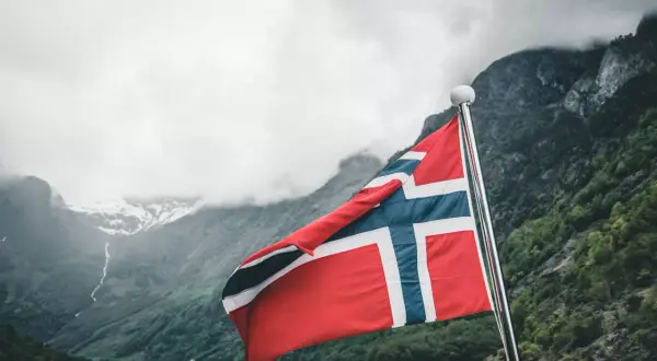 Flaga Norwegii powiewa na maszcie na tle malowniczego fiordu.