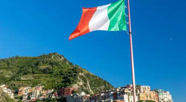 Flaga Włoch powiewa na tle błękitnego nieba nad kolorowymi domkami Cinque Terre.