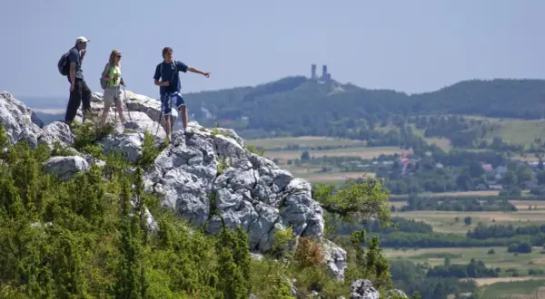 Trzech turystów na skale podziwia krajobraz. W oddali widać ruiny zamku i malownicze kielce góry.