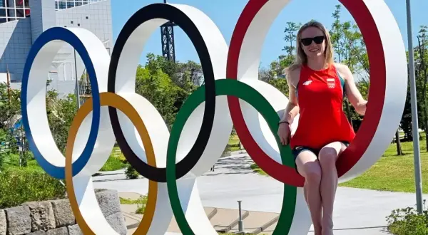 Kobieta w czerwonej koszulce z polską flagą siedzi na jednym z kół symbolizujących flagę olimpijską.