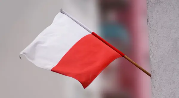 Flaga Polski powiewa na wietrze, biało-czerwona, ale w odwrotnej kolejności.