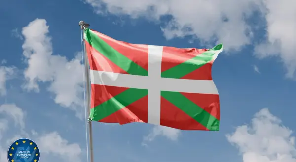 Flaga Basków (Ikurriña) powiewa na tle błękitnego nieba z chmurami.