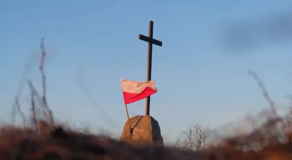 Na kamieniu, pod krzyżem, powiewa biało-czerwona flaga Polski.