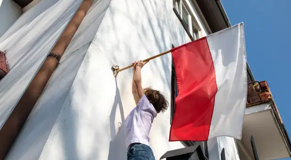 Dziecko zdejmuje biało-czerwoną flagę. Zgodnie z tradycją, flagę zdejmuje się po 3 maja, gdy minie czas jej wywieszenia.