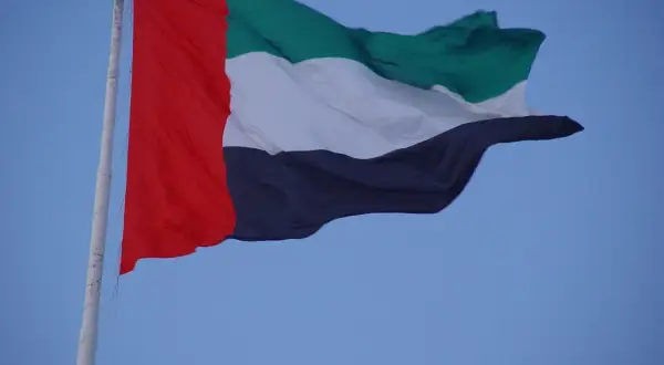 Flaga Zjednoczonych Emiratów Arabskich, znana również jako flaga Dubaju, powiewa na maszcie na tle błękitnego nieba.