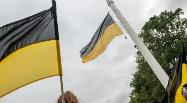 Flaga Kaszub powiewa na maszcie. Dwie flagi w kolorach czarnym i żółtym, symbolizujące Kaszuby, są widoczne na tle pochmurnego nieba.