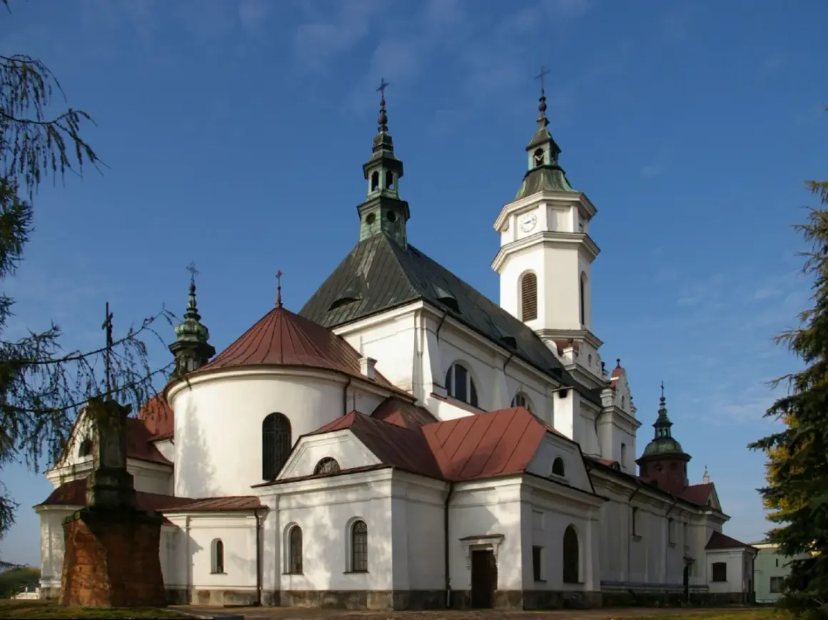 Kościół z wieżą zegarową i krzyżami na tle błękitnego nieba.