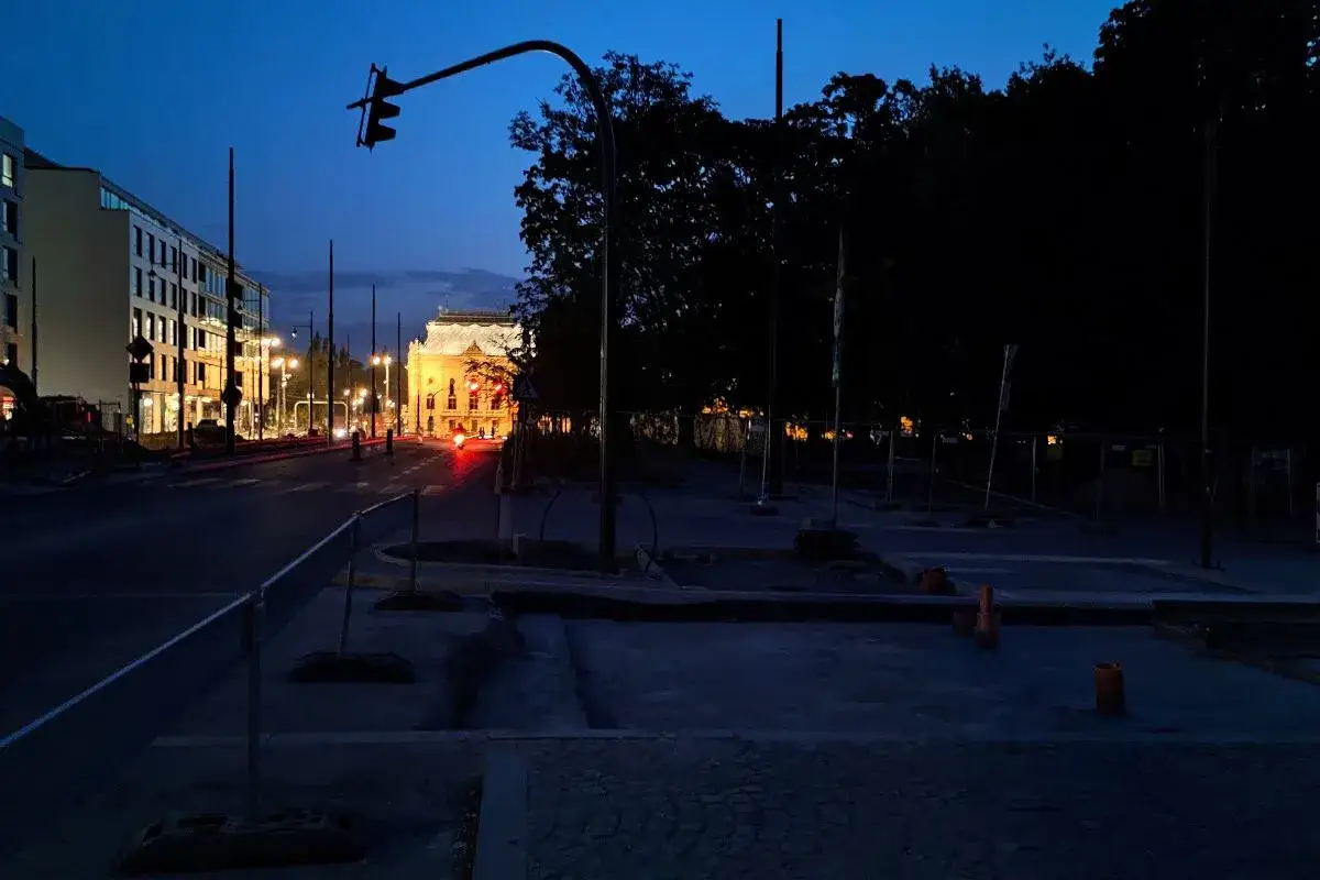 Zmierzch w mieście. Ulica z sygnalizacją świetlną i budynkami. Czy łódź jest bezpieczna? Teren budowy z pomarańczowymi pachołkami.