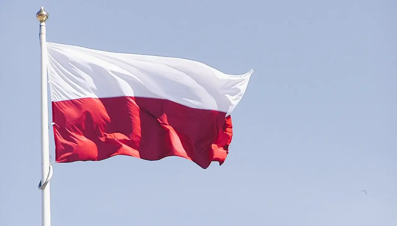 Biało-czerwona flaga Polski powiewa na maszcie. Biały pas jest na górze, a czerwony na dole, co jest prawidłowym ułożeniem.