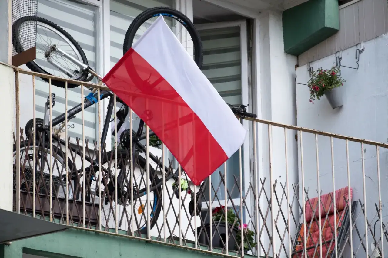 Polski biało-czerwony symbol narodowy dumnie powiewa na balkonie, przypominając o ważnych datach, kiedy wywieszamy flagę. Obok rower i kwiaty.