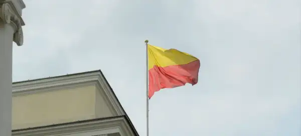 Flaga Warszawy powiewa na maszcie obok zabytkowego budynku.