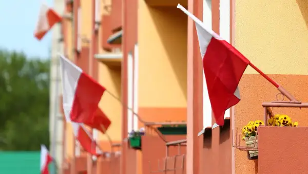 Kilka biało-czerwonych flag państwowych powiewa na tle pomarańczowo-żółtego budynku.