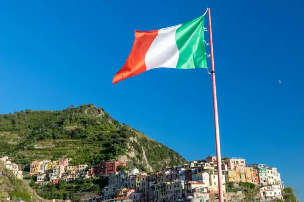 Flaga Włoch powiewa na tle błękitnego nieba nad kolorowymi domkami Cinque Terre.