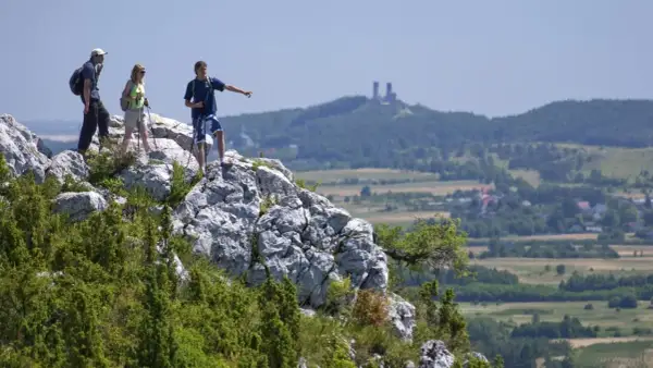 Trzech turystów na skale podziwia krajobraz. W oddali widać ruiny zamku i malownicze kielce góry.