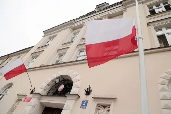 Flaga Polski pionowo powiewa przed budynkiem. Biało-czerwone barwy dumne na tle jasnej fasady.