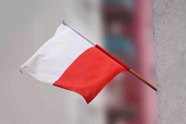 Flaga Polski powiewa na wietrze, biało-czerwona, ale w odwrotnej kolejności.