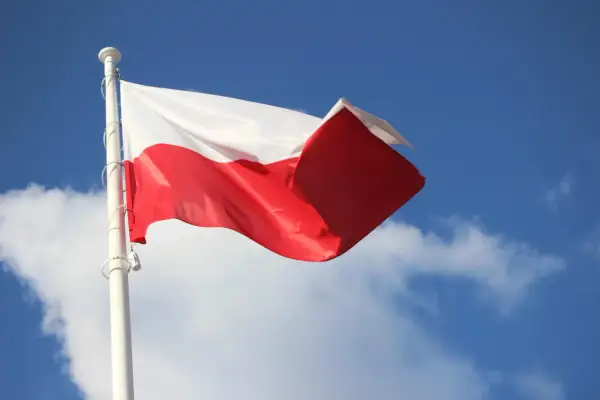 Biało-czerwona flaga Polski powiewa na maszcie na tle błękitnego nieba z chmurami. To symbol ważnych dat, kiedy wywieszamy flagę.