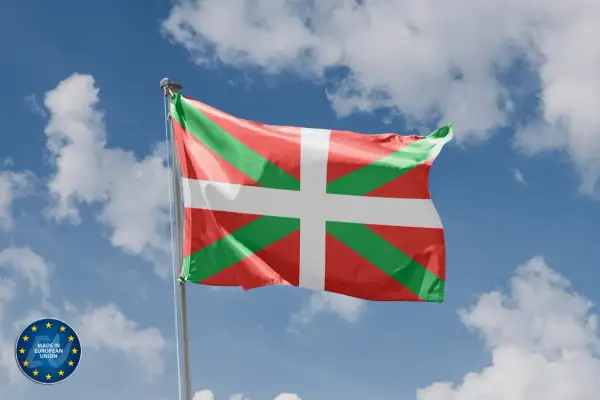 Flaga Basków (Ikurriña) powiewa na tle błękitnego nieba z chmurami.