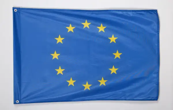 Niebieska flaga z dwunastoma złotymi gwiazdami ułożonymi w okrąg. To godło Unii Europejskiej, symbol jedności i solidarności.